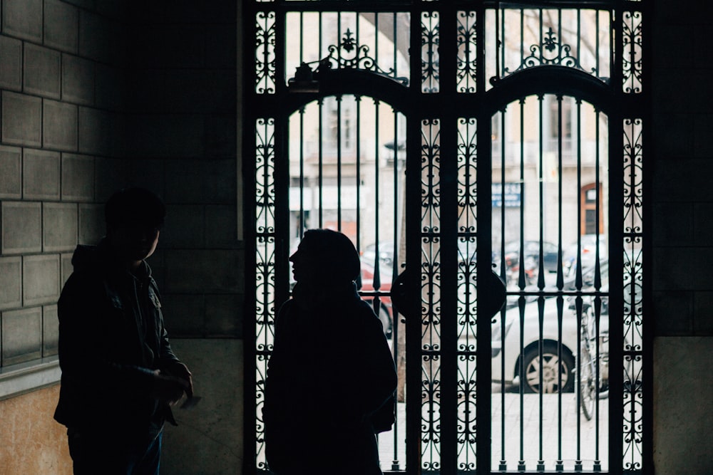 silhouette of two persons standing beside gate