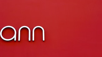 A minimalistic design displays the letters 'ann' in a sleek, modern font against a deep red background.