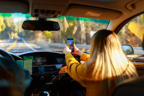 A happy traveler filling out an outstation booking form on a smartphone, with a scenic road in the background.
