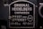 A metal plaque with the text 'Original Heidelberg Einfarben Offset oder Letterset' and measurements '46x62 cm' and '18x24½'. The background of the plaque is dark, and the text and borders are in a lighter metallic color.