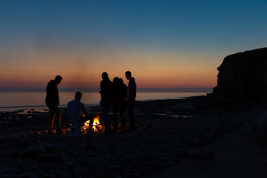 Campers silhouetted around a bonfire at night