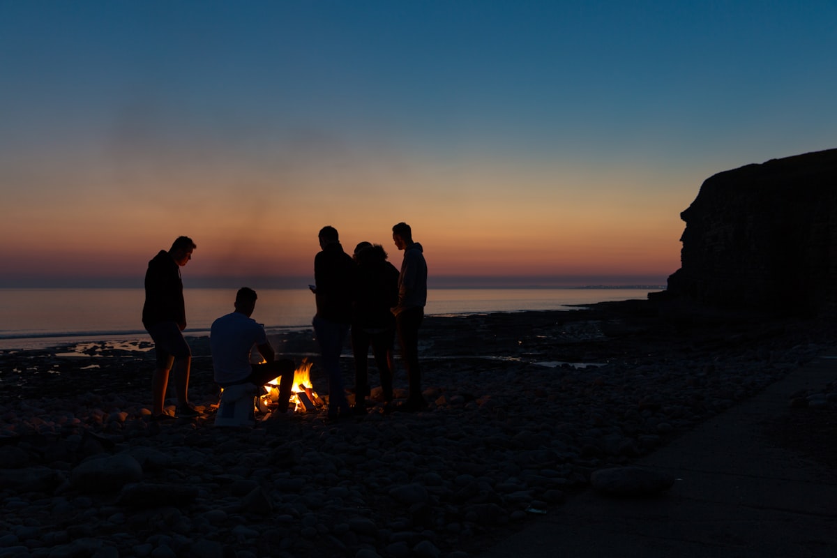 Boys on a beach standing around a lit signal fire at dusk