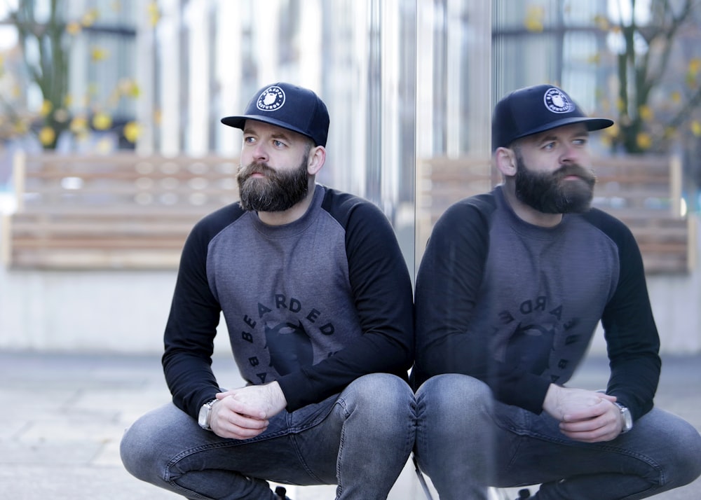 man in gray and black raglan sitting beside glass wall