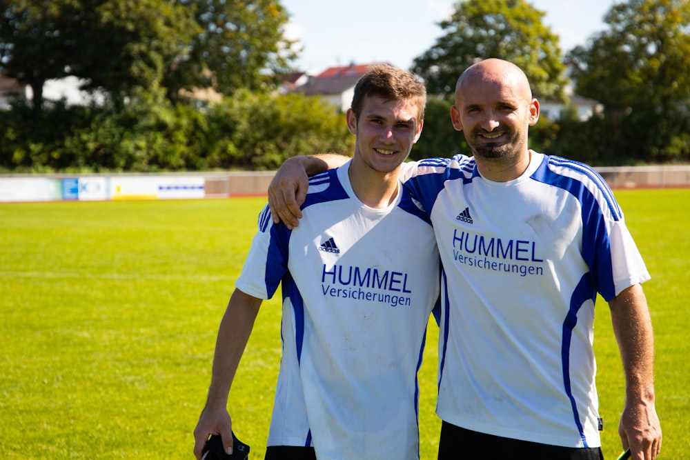 two smiling men standing in green field