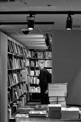 A person stands in a bookstore aisle, focused on shelves filled with various art books. The environment is well-lit with overhead lights and the books are organized neatly on the shelves.