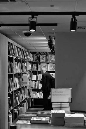A person stands in a bookstore aisle, focused on shelves filled with various art books. The environment is well-lit with overhead lights and the books are organized neatly on the shelves.