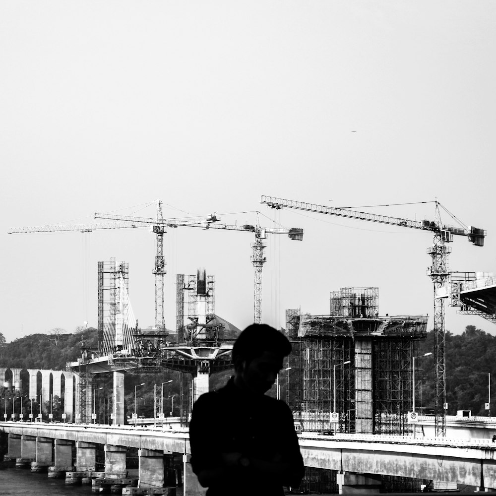 Fotografía en escala de grises de un hombre con un sitio de construcción en el fondo