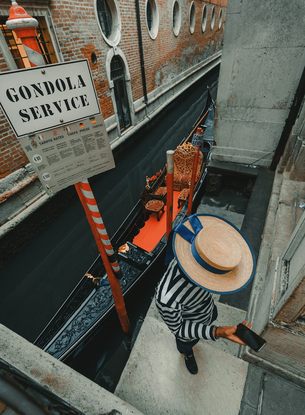 persona que usa el teléfono mientras está de pie cerca de la góndola junto al canal de Venecia durante el día