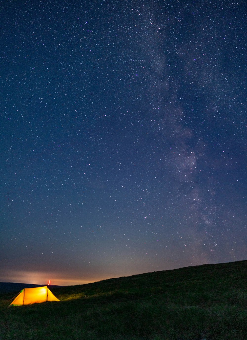 a tent pitched up on a grassy hill under a night sky filled with stars