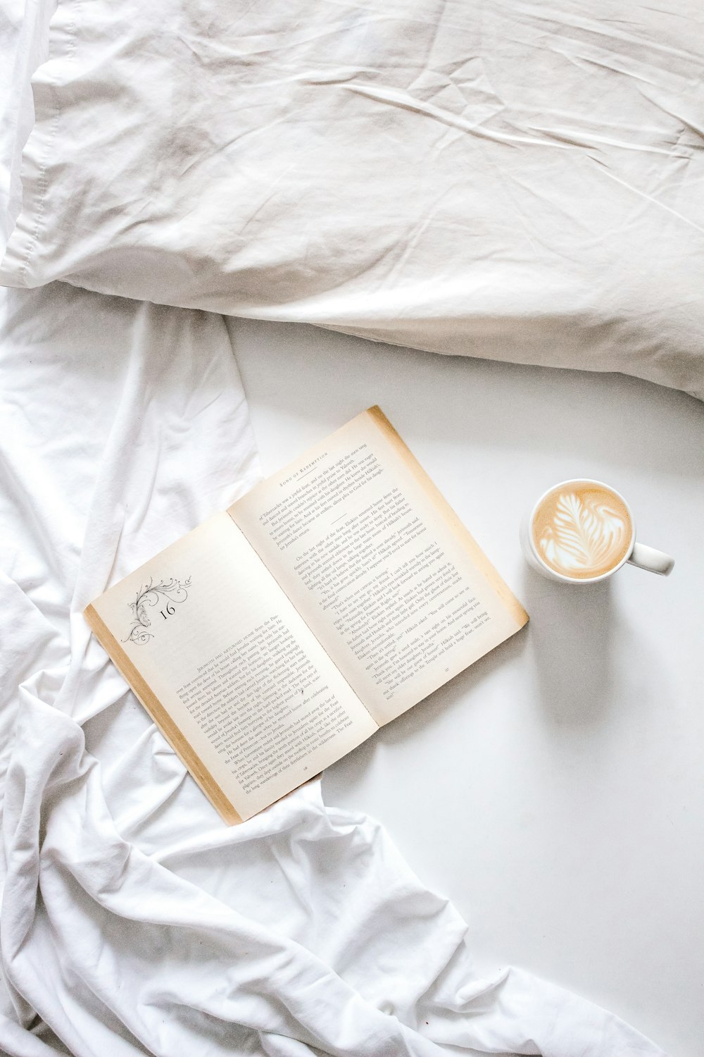 open book beside cup of coffee on bed