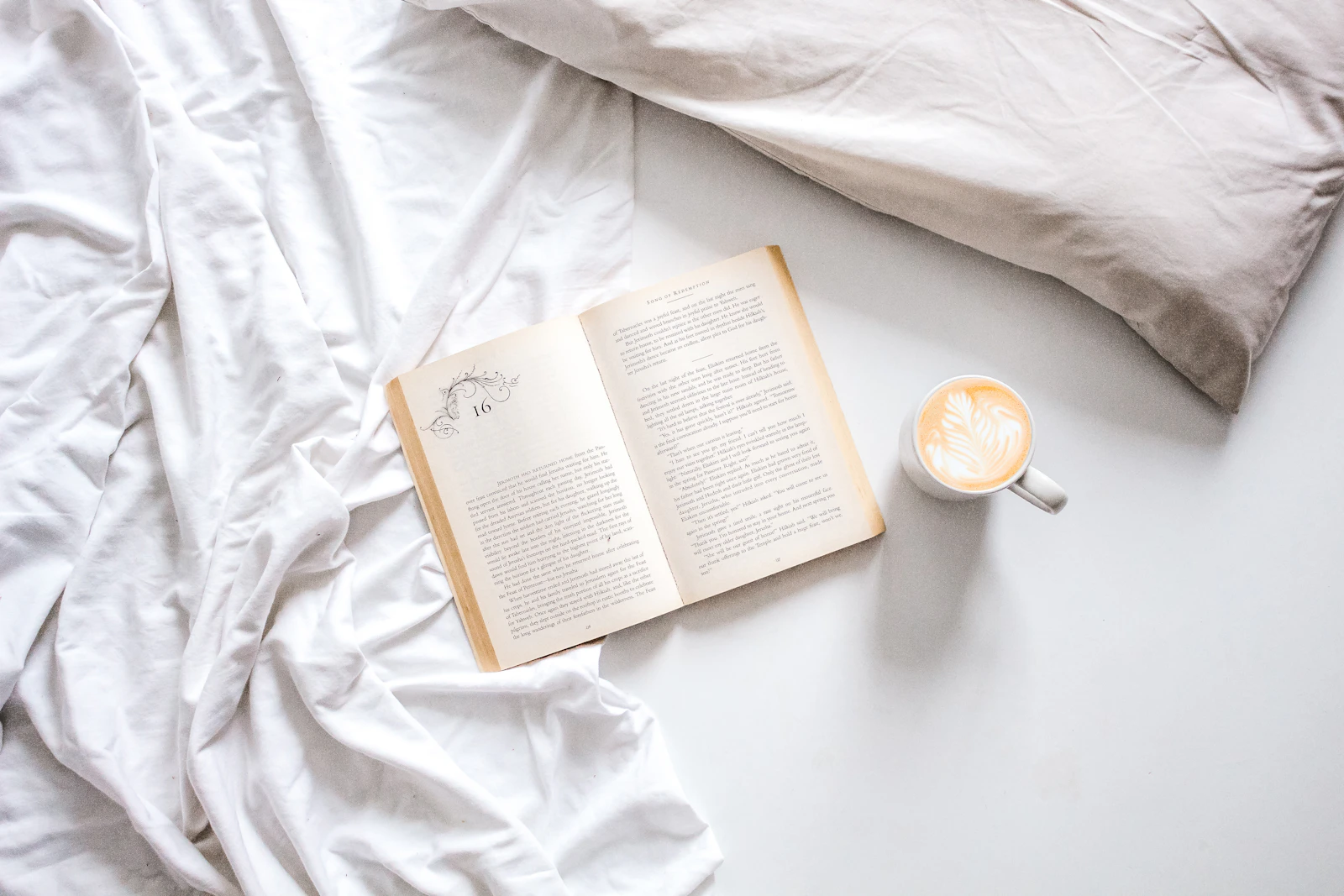 Flat-lay of an open book and a mug of coffee resting on linen sheets