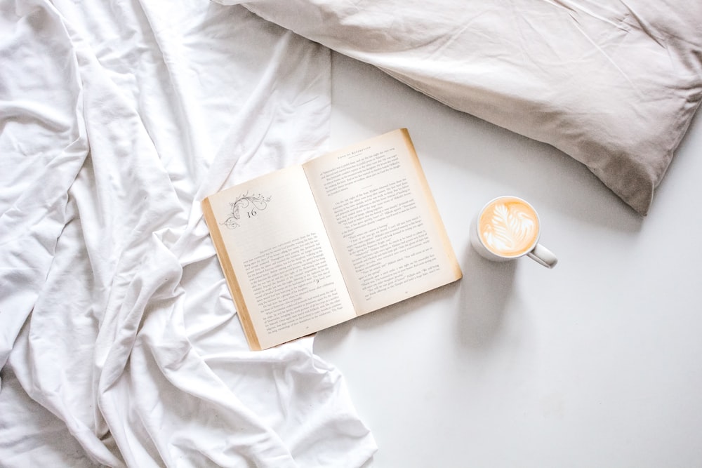 flat-lay photography of an open book and mug of coffee in bed