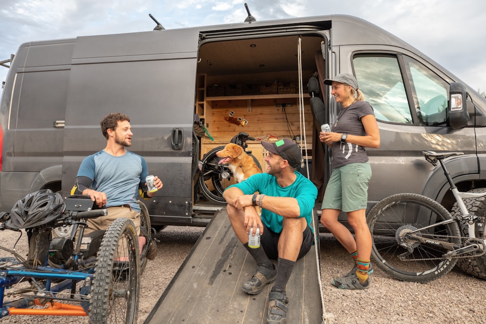 two men and one woman sitting beside van