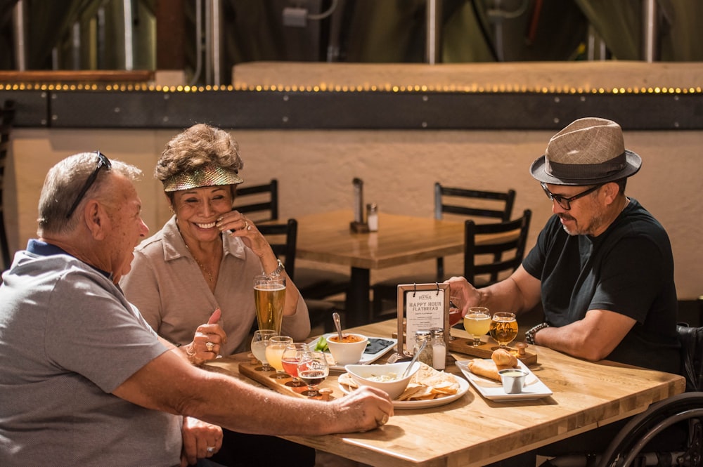Drei lächelnde Menschen sitzen neben einem Tisch mit einem Teller mit Speisen und Getränken