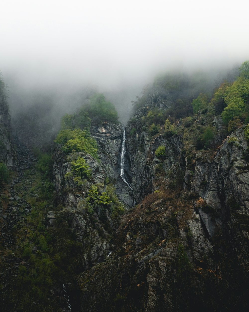 a waterfall in the middle of a mountain surrounded by fog