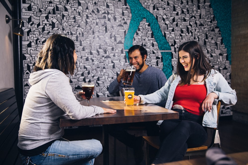 homem rindo sentado perto de duas mulheres ao lado da mesa de madeira