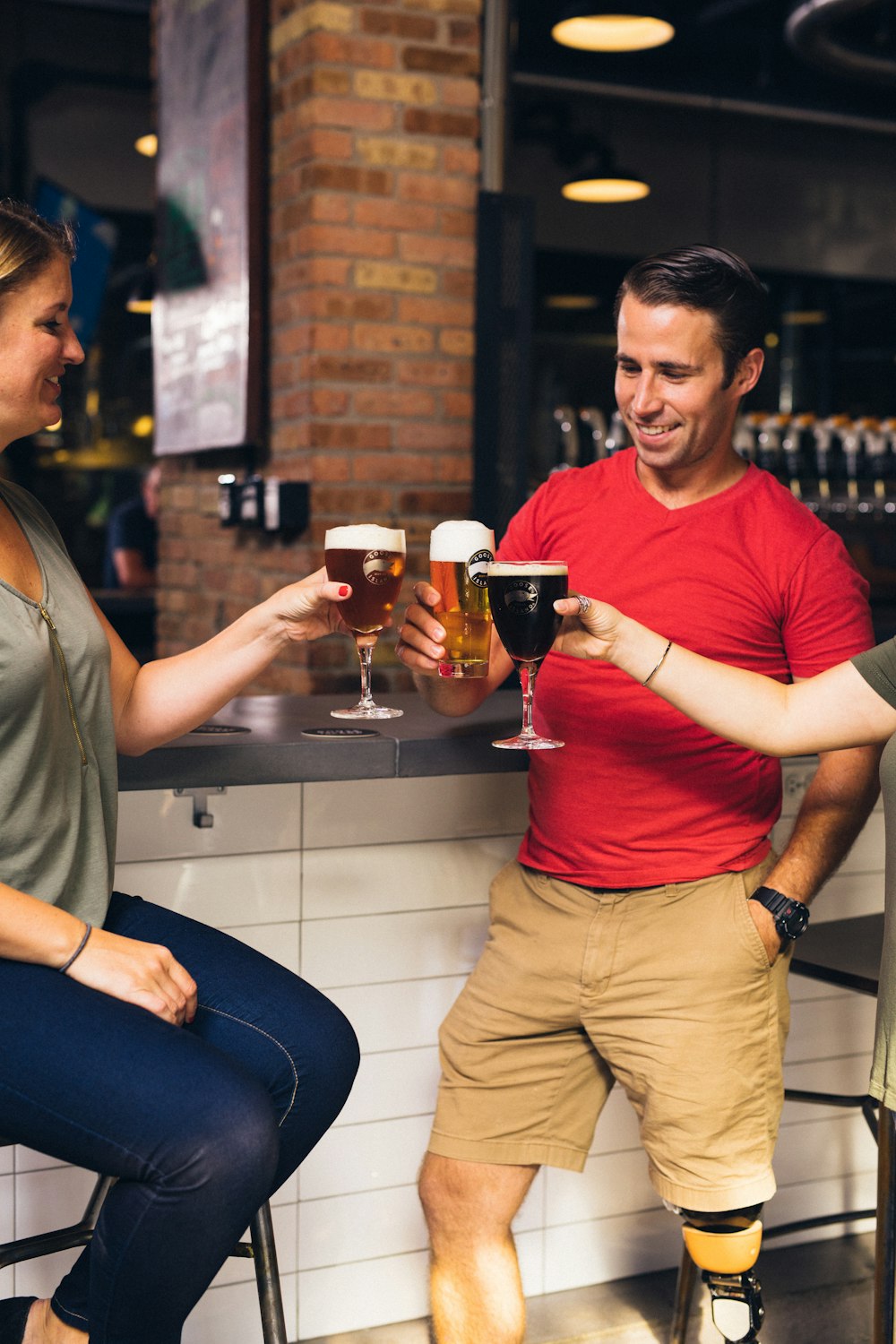 Mujer sentada en el taburete de la barra cerca de otras dos personas brindando cerveza