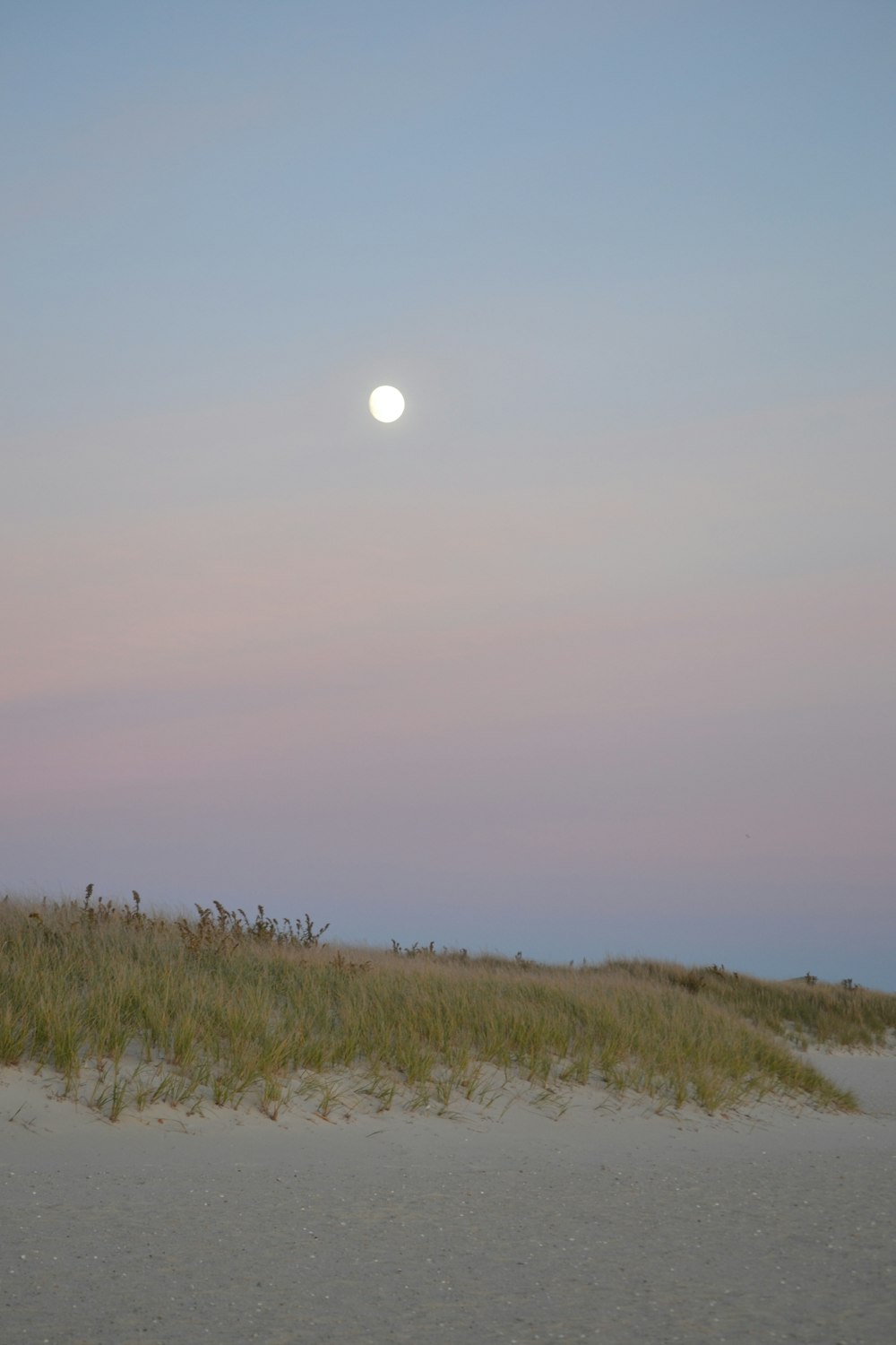 the sun is setting over the beach and grass