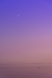a purple sky with a half moon in the distance