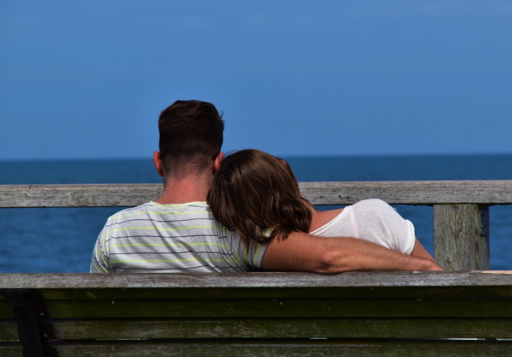 man and woman sitting on bench near body of water during daytime