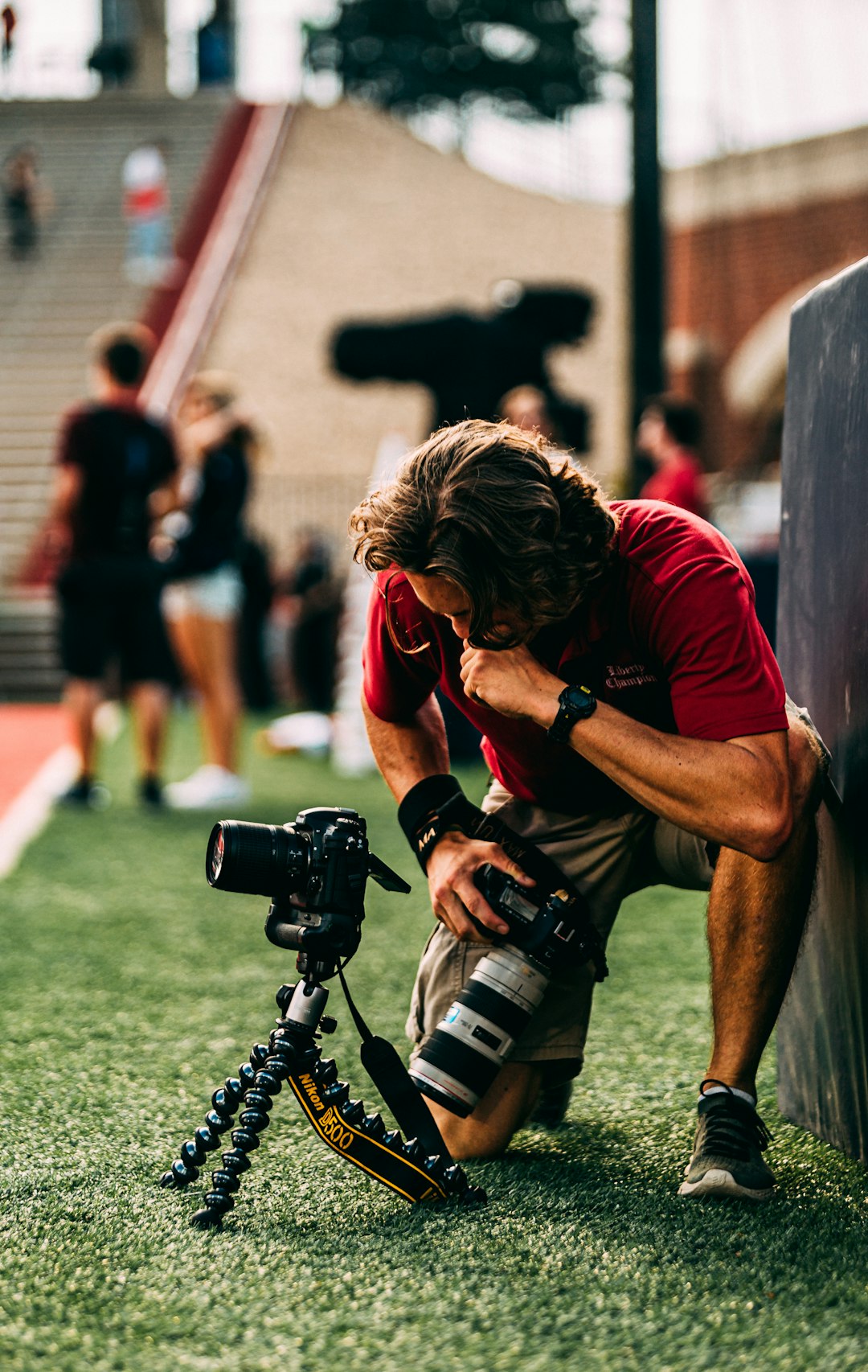 man kneeling on grass field holding DSLR camera