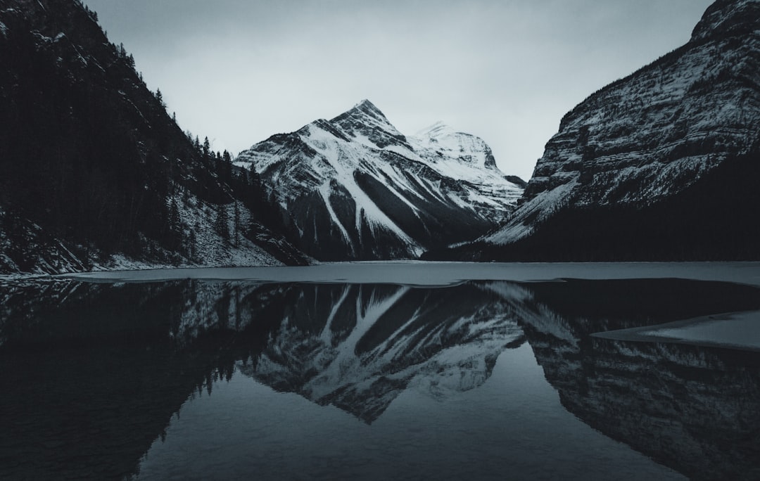 grayscale photo of snow covered mountain, Beautiful reflections in a moody lake in front of a snowy mountain in the Rock