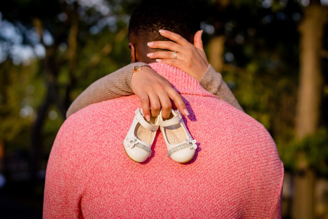 woman hugging man while holding baby shoes