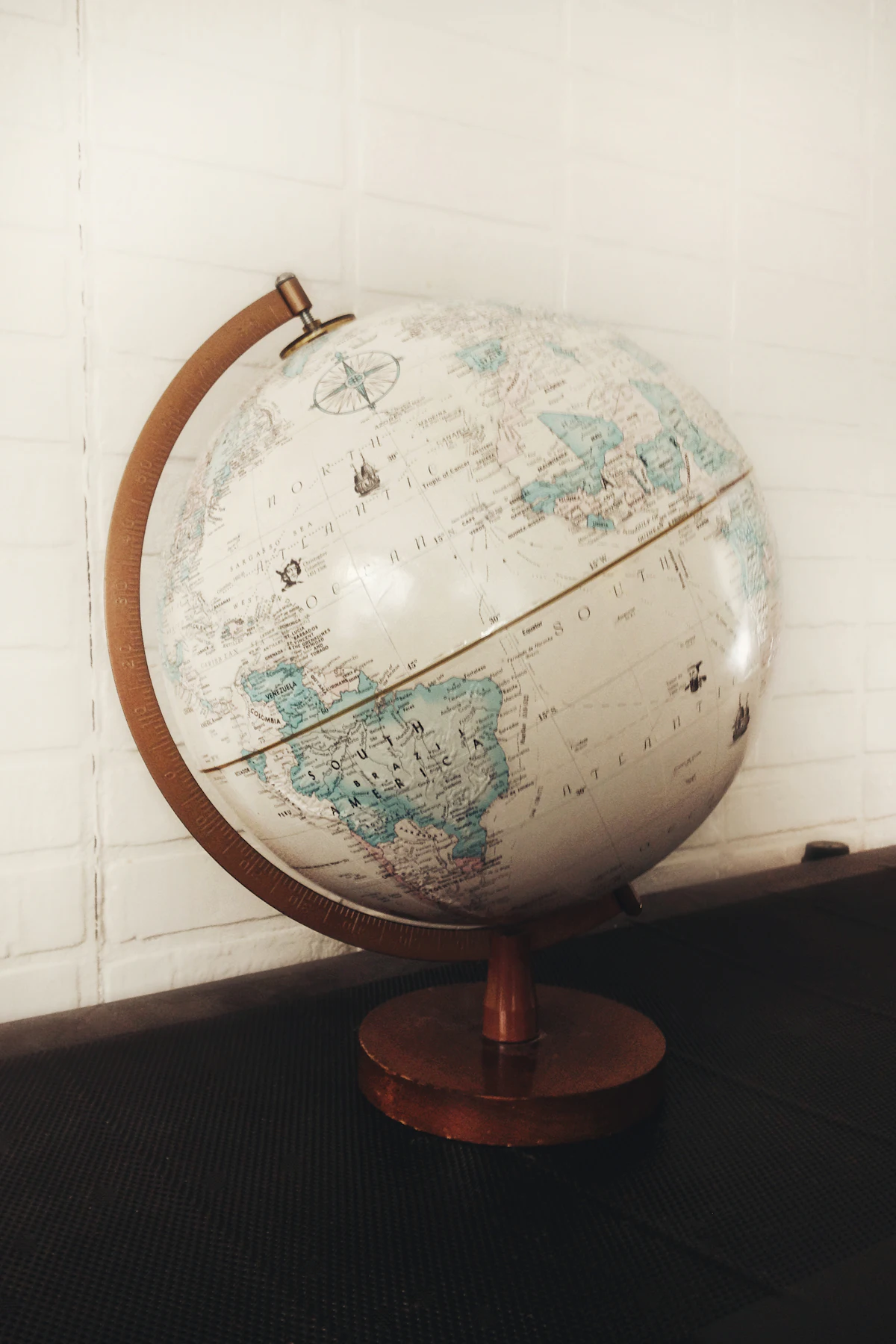 A vintage desk globe on a wooden stand against a white brick wall