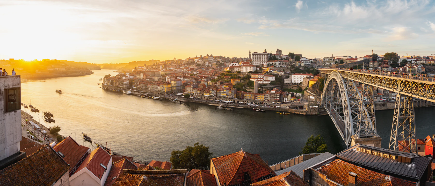 Photograph of Porto and Vila Nova de Gaia rise on both banks of the Douro around Dom Luís I Bridge in warm evening light.