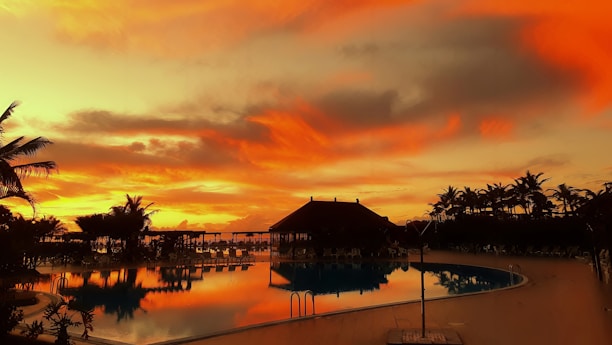 A breathtaking resort at sunset with a calm ocean and palm trees framing the scene.