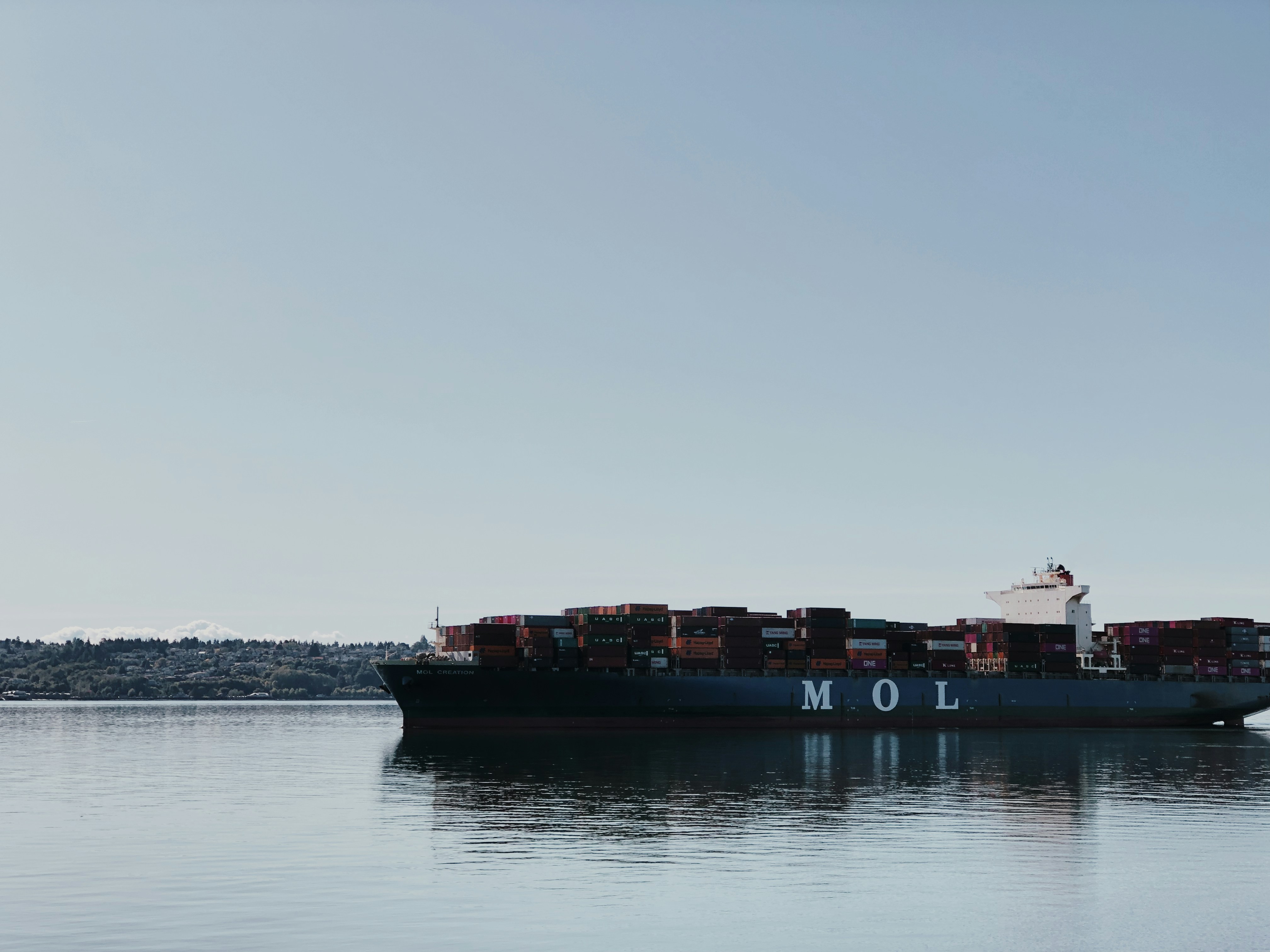 A large cargo ship with colorful containers stacked high, sailing calmly across the ocean under a clear blue sky.