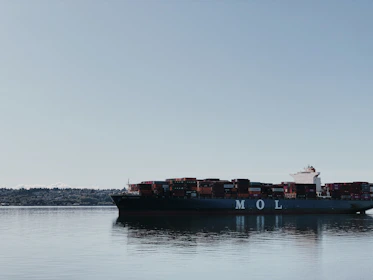 A large cargo ship loaded with colorful containers sailing on calm ocean waters under a clear sky.