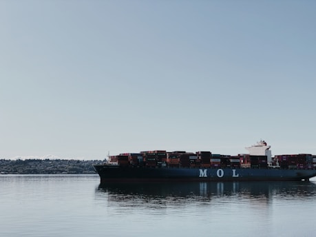 A large cargo ship loaded with colorful containers sailing on a calm blue ocean under a clear sky.