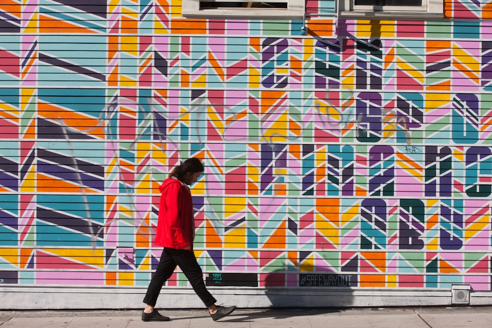 woman in red hoodie walking beside wall