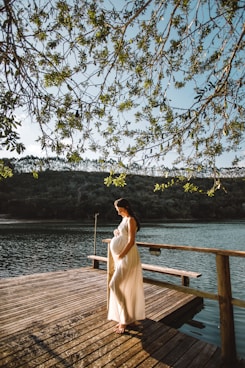 pregnant woman standing on wooden dock under tree