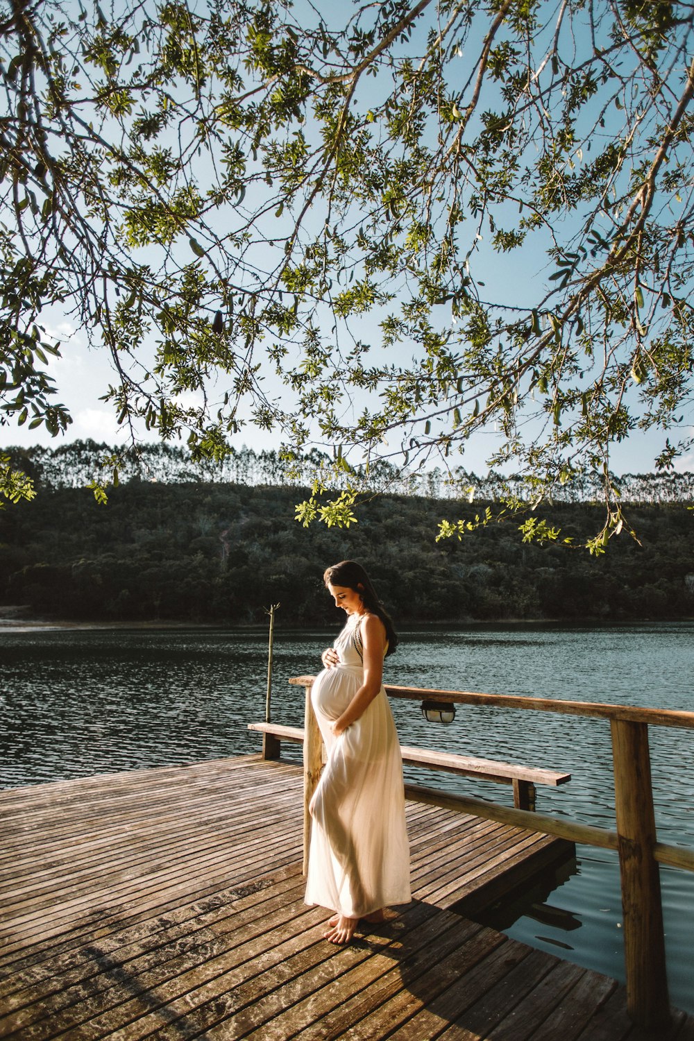 pregnant woman standing on wooden dock under tree