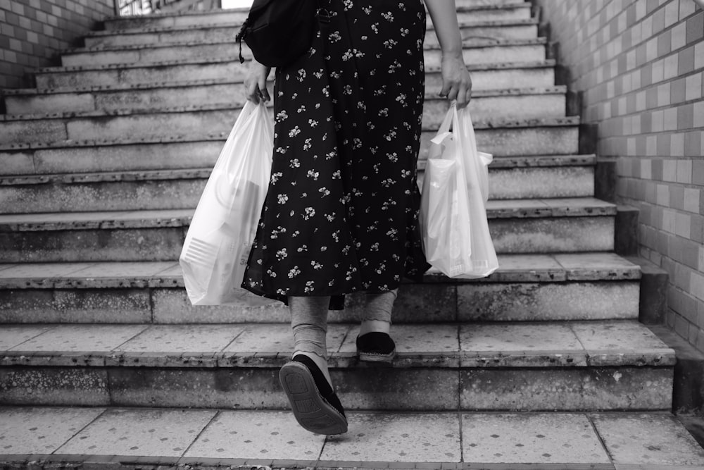 grayscale photography of person holding plastic bags walking on concrete stairs going up