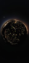 A spherical 360-degree view of a city at night, with illuminated streets and buildings forming a circular pattern. In the background, a bright celestial body is visible in the dark sky, adding a cosmic element to the scene.