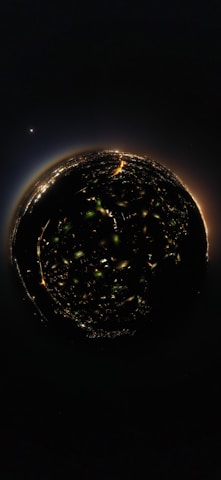 A spherical 360-degree view of a city at night, with illuminated streets and buildings forming a circular pattern. In the background, a bright celestial body is visible in the dark sky, adding a cosmic element to the scene.
