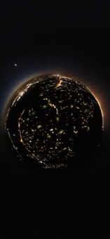 A spherical 360-degree view of a city at night, with illuminated streets and buildings forming a circular pattern. In the background, a bright celestial body is visible in the dark sky, adding a cosmic element to the scene.