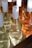 Several bottles of wine are neatly arranged in a wooden tray, showcasing both clear and amber liquids. Each bottle features a white cap and a minimalist design. The sunlight casts a bright reflection on the glass, enhancing the clarity and highlights of the bottles.