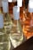 Several bottles of wine are neatly arranged in a wooden tray, showcasing both clear and amber liquids. Each bottle features a white cap and a minimalist design. The sunlight casts a bright reflection on the glass, enhancing the clarity and highlights of the bottles.