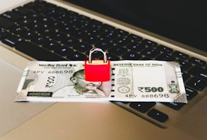 An Indian 500 rupee note is placed on a laptop keyboard with a red padlock sitting on top of the note.