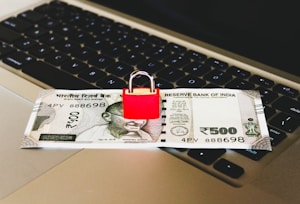 An Indian 500 rupee note is placed on a laptop keyboard with a red padlock sitting on top of the note.
