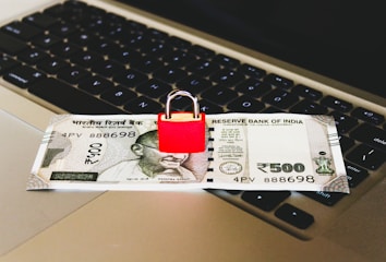 An Indian 500 rupee note is placed on a laptop keyboard with a red padlock sitting on top of the note.