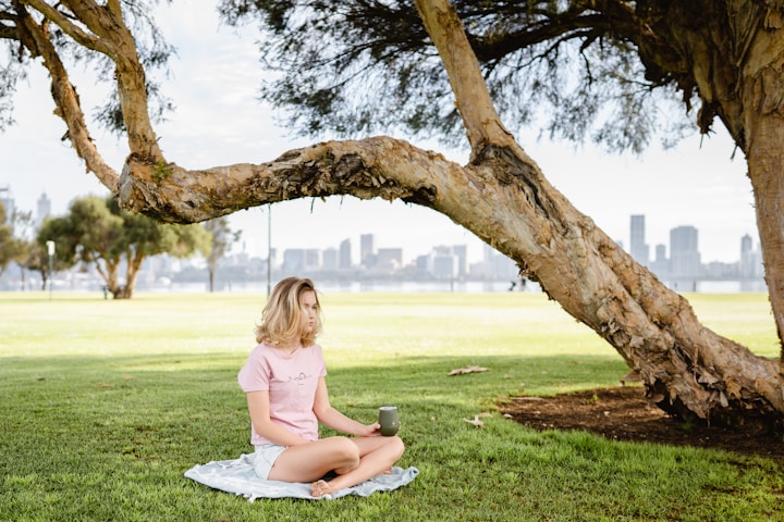 mulher sentada meditando embaixo de uma árvore com foco na fotografia