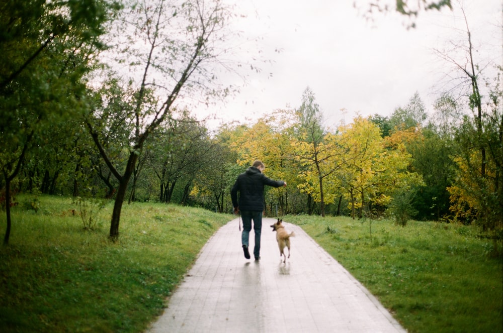 man beside dog walking in pathway surrounded by trees