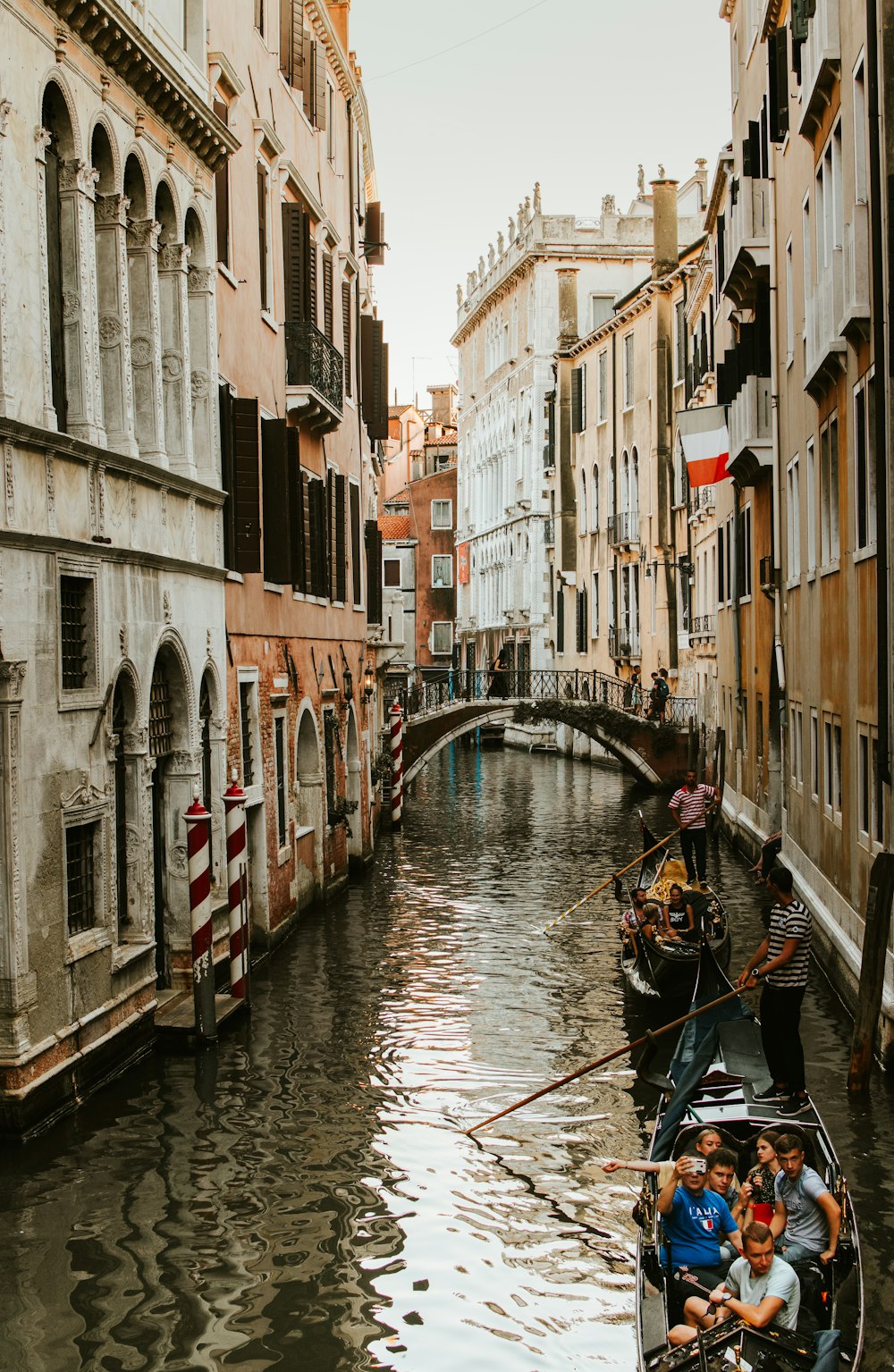 people riding boats floating on canal between buildings