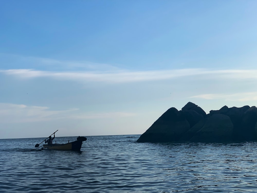 person in boat on body of water viewing mountain under blue and white skies during daytime