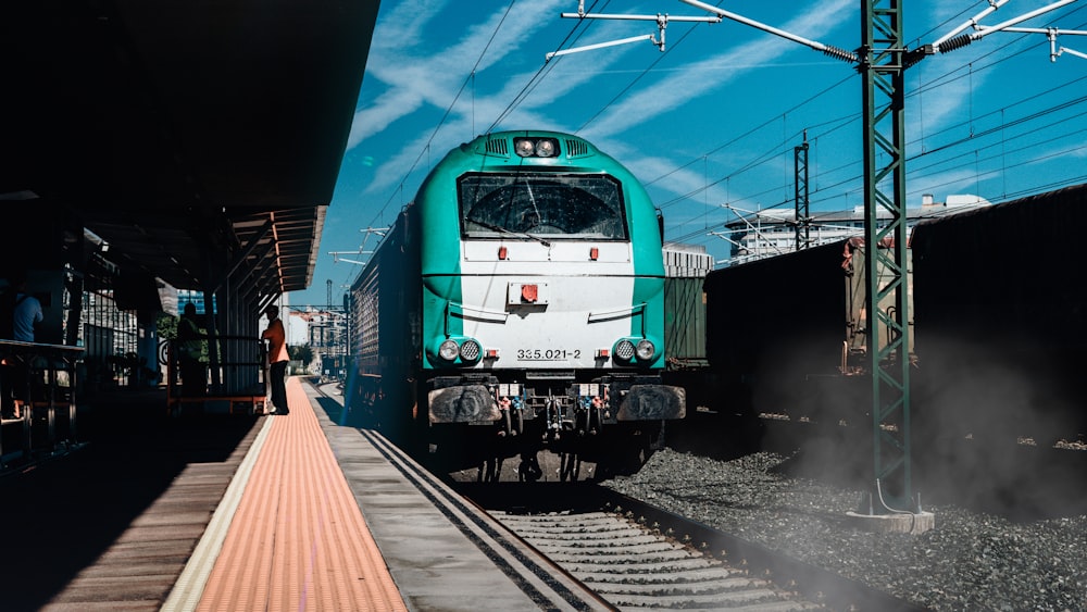 a green and white train pulling into a train station